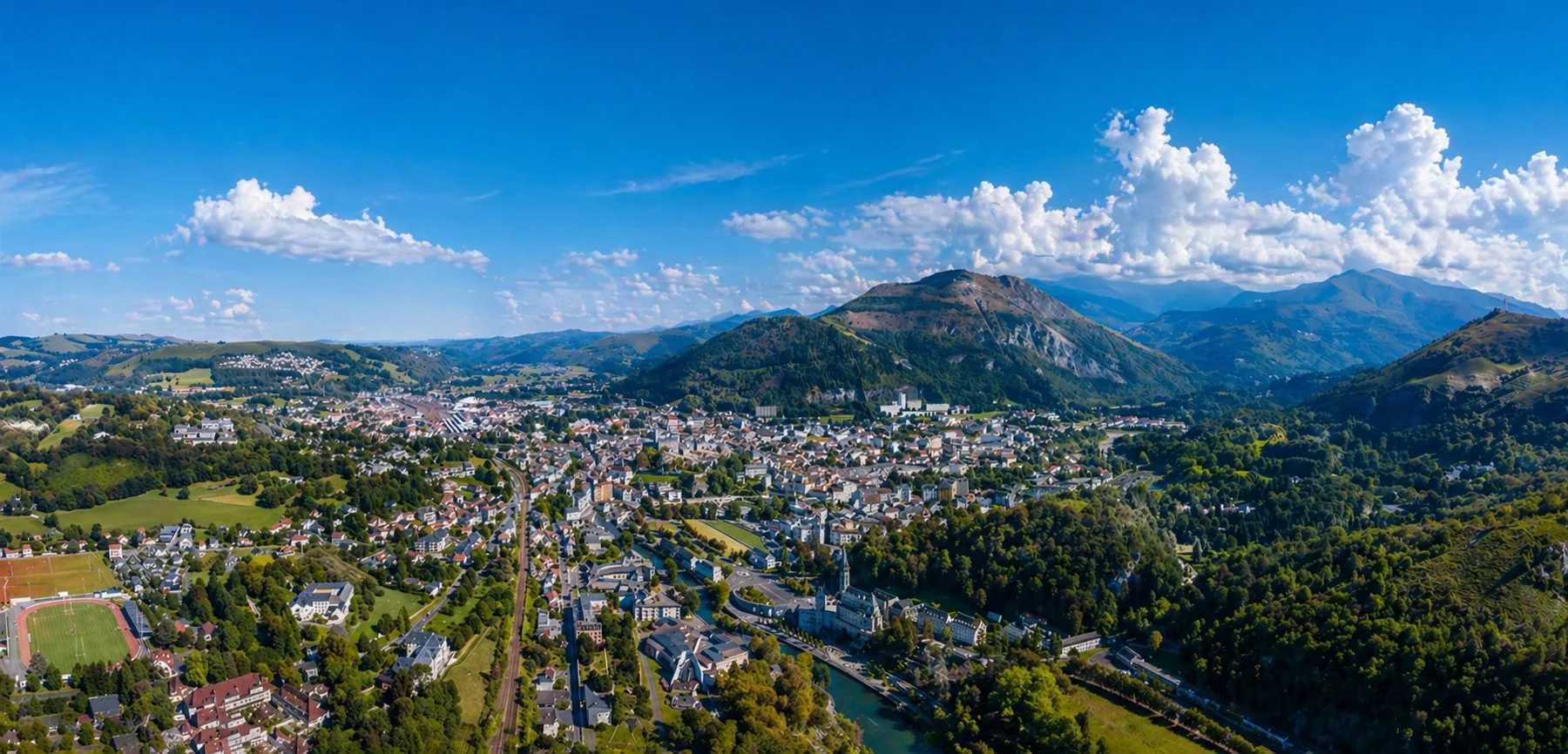 Vue aérienne panoramique de Lourdes avec le Sanctuaire, la ville, les reliefs et les Pyrénées